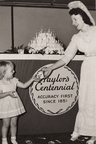 Centennial Cake & Ice Cream Treat Hostess in 1851 period attire serving ice cream to a young guest in front of the multi-tiered 100th anniversary cake.